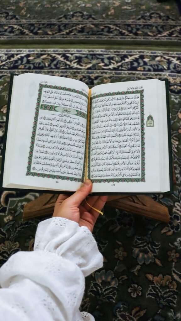 A person holds an open Quran in a mosque setting, symbolizing devotion and faith.