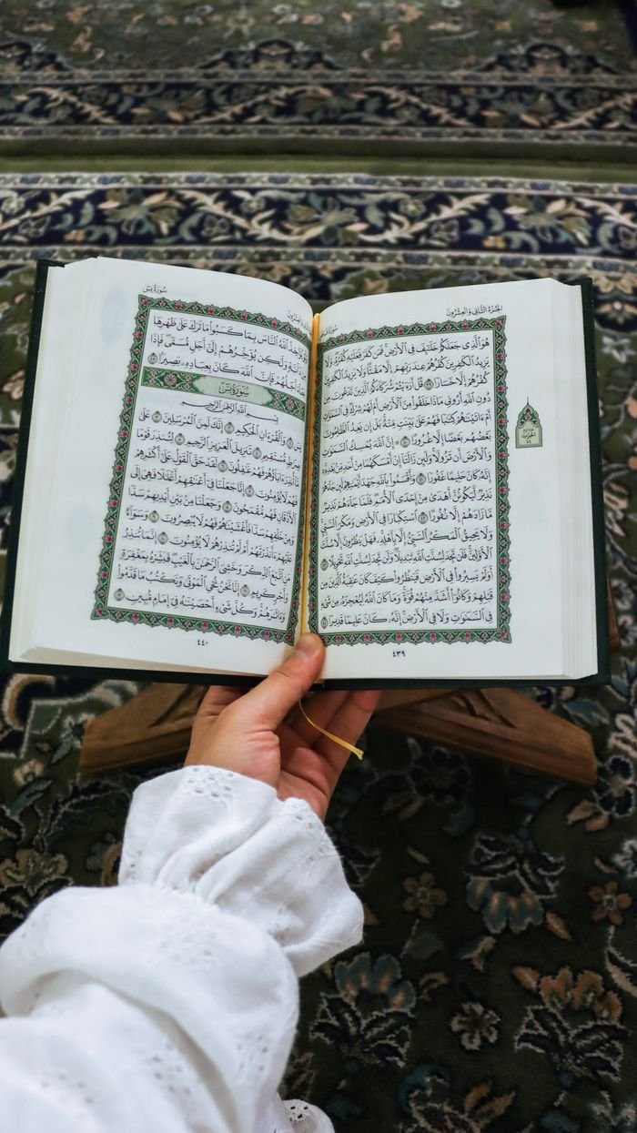 A person holds an open Quran in a mosque setting, symbolizing devotion and faith.