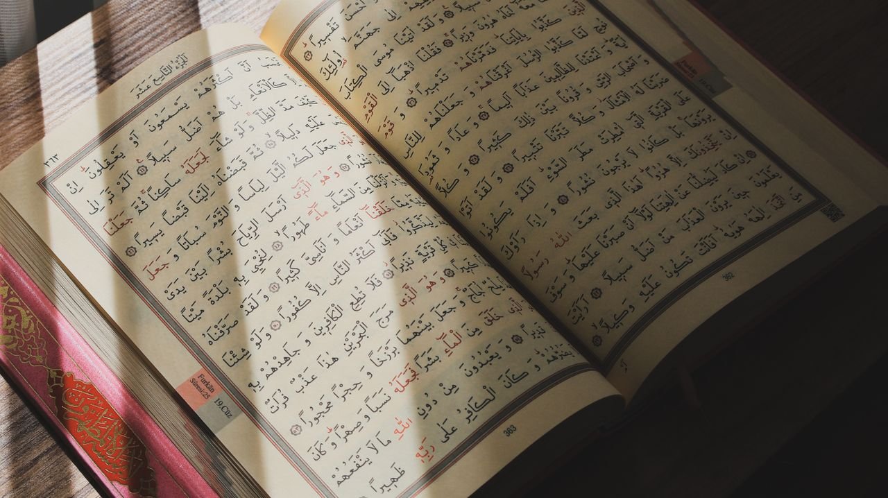 An open Quran with Arabic script illuminated by natural sunlight on a wooden surface.