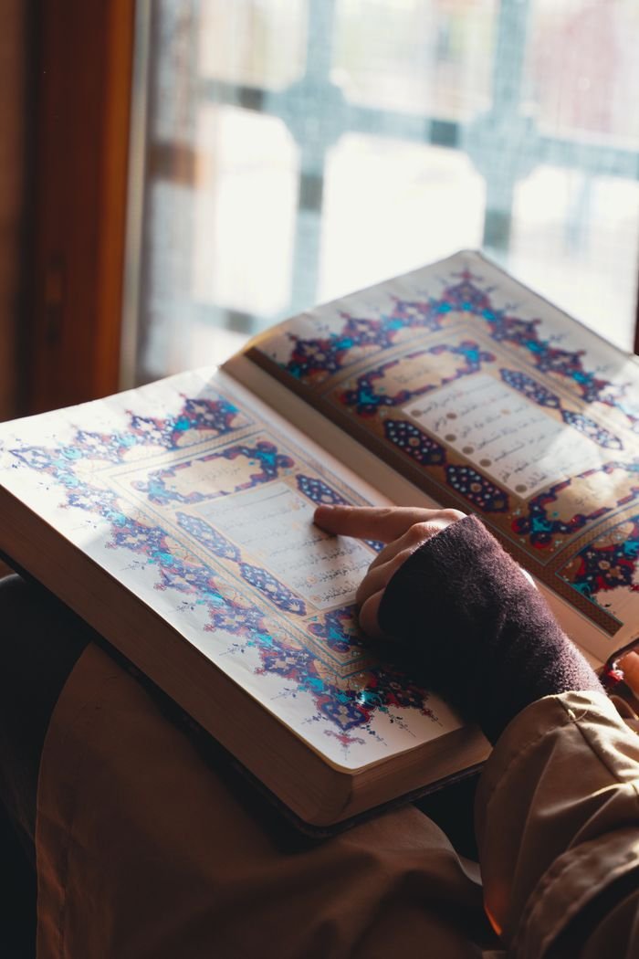 Person engaging with the Quran by a sunlit window in Adana, Türkiye.